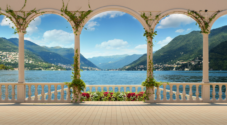 Ein eleganter Balkon mit Steinbalustrade und Blumen bietet einen weiten Blick auf den Comer See und die umliegenden Berge
