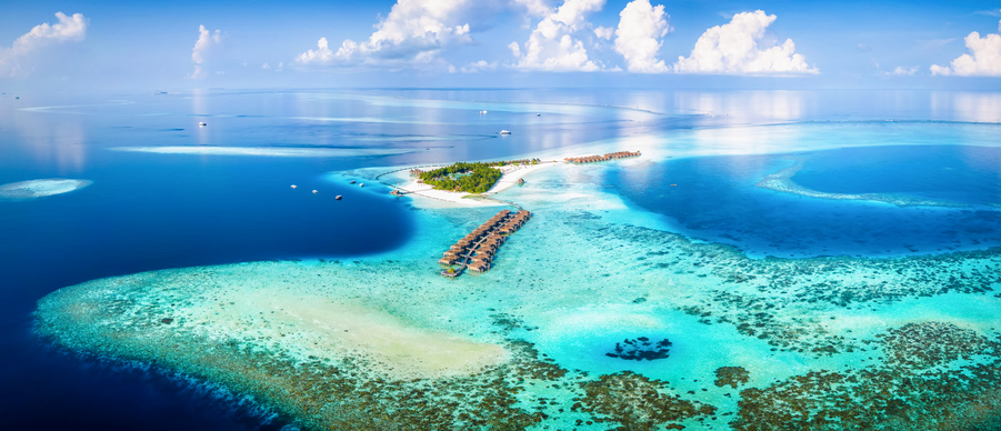 Panorama-Luftaufnahme einer kleinen Insel mit luxuriösen Bungalows im türkisfarbenen Atoll-Wasser
