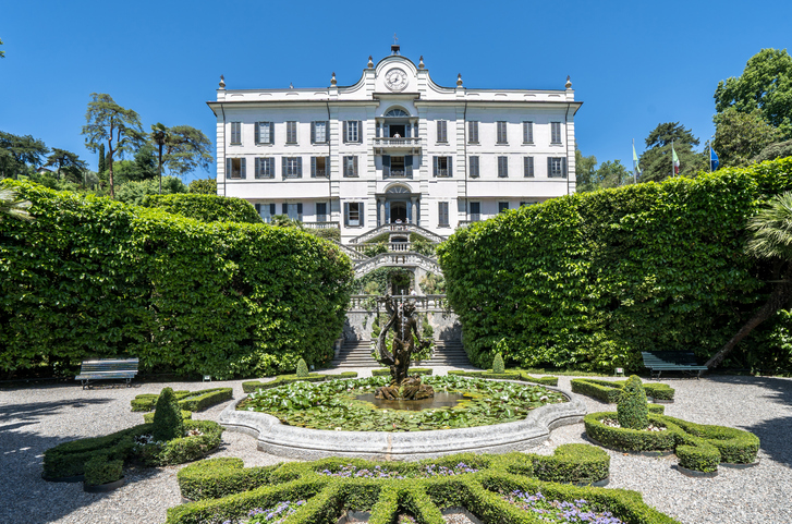 Ein kunstvoller Springbrunnen in einem gepflegten Garten vor einer eleganten weißen Villa am Comer See
