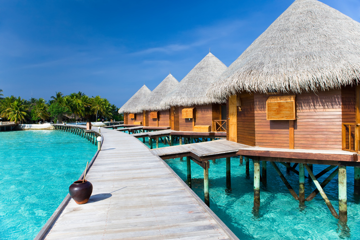 Reihe von Wasserbungalows mit Strohdächern über türkisblauem Wasser auf den Malediven