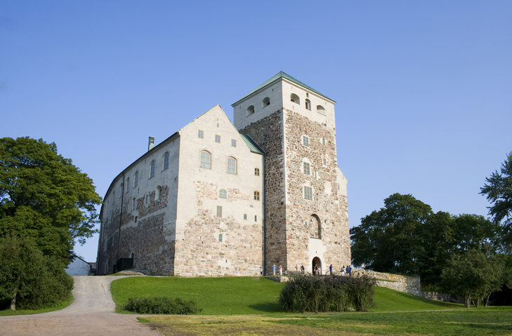 Eine massive, helle Steinfestung mit quadratischem Turm, die Burg Turku, unter strahlend blauem Himmel.