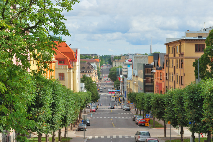 Eine weite Straße in Turku mit historischen nordischen Holzhäusern und moderneren Gebäuden unter bewölktem Himmel.