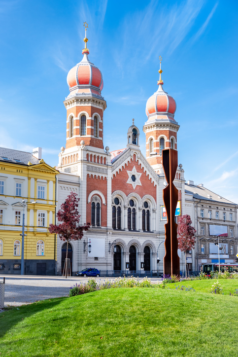 Die imposante Große Synagoge von Pilsen mit ihren zwei markanten Zwiebeltürmen und der roten Backsteinfassade unter blauem Himmel.