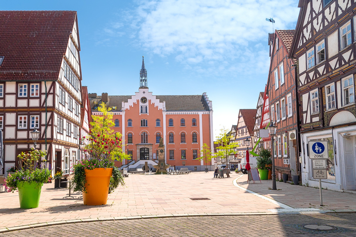 Ein weiter Pflasterplatz mit einem rosafarbenen Rathaus im Hintergrund, gesäumt von gepflegten Fachwerkhäusern.