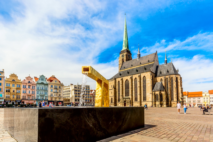Blick über den Marktplatz auf die gotische Kathedrale und einen modernen, goldenen Brunnen im Vordergrund.