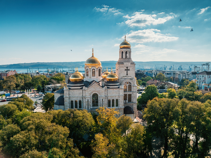 Luftaufnahme der monumentalen Kathedrale Mariä Himmelfahrt in Warna mit ihren leuchtend goldenen Kuppeln unter blauem Himmel.