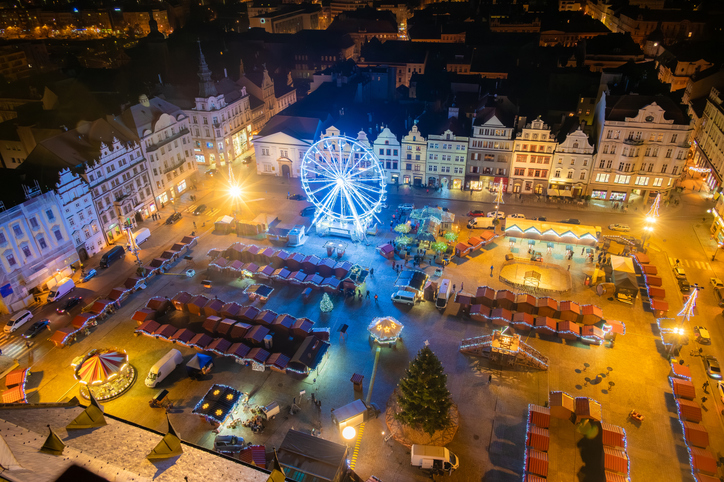 Blick von oben auf den beleuchteten Marktplatz von Pilsen mit einem blauen Riesenrad, Weihnachtsmarkt-Hütten und einem großen Tannenbaum.