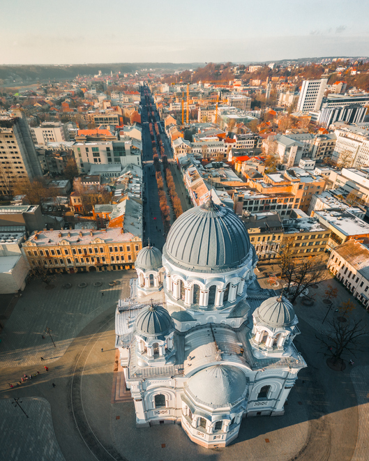 Blick von oben auf die imposante weiß-blaue Kuppelkirche am Ende der von Bäumen gesäumten Laisvės alėja.