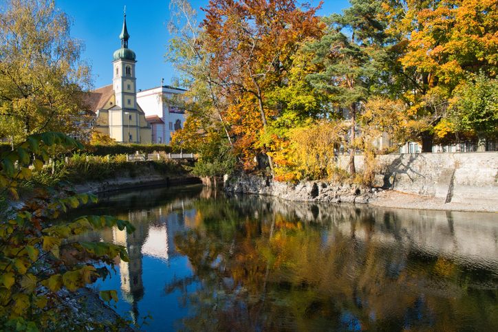 Ein ruhiger Flussarm in Konstanz mit Spiegelungen von herbstlich gefärbten Bäumen und einem Kirchturm im Wasser.