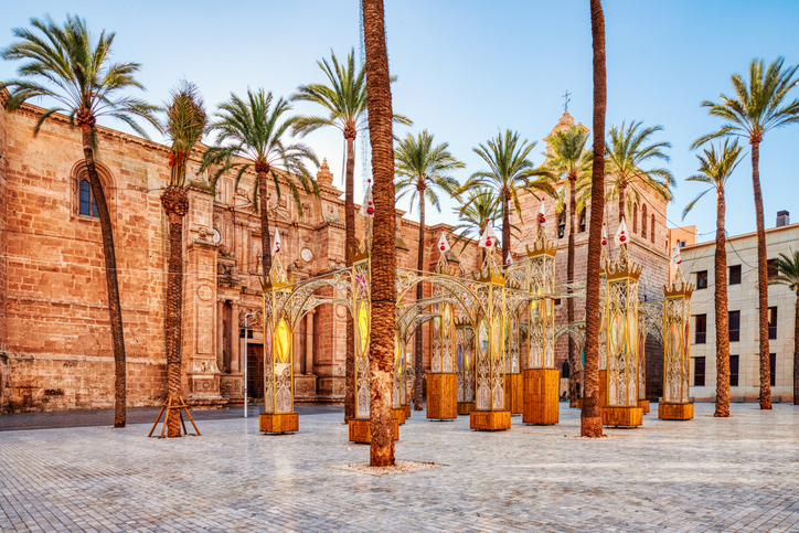 Ein weiter, gepflasterter Platz mit hohen Palmen vor der massiven Steinfassade der Kathedrale von Almería.