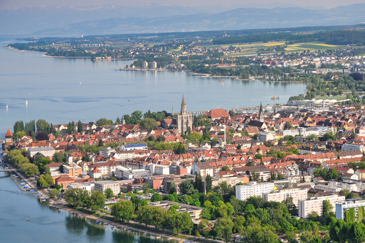 Blick aus der Vogelperspektive auf die dicht bebaute Altstadt von Konstanz, die direkt an das tiefblaue Wasser grenzt.