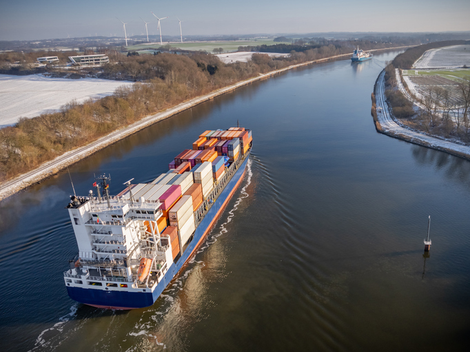Ein großes Containerschiff fährt auf dem Nord-Ostsee-Kanal durch eine ruhige Winterlandschaft nahe Kiel.