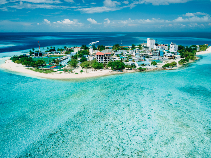 Luftaufnahme einer bewohnten Insel auf den Malediven mit Häusern, Bäumen und umgeben von flachen Korallenriffen