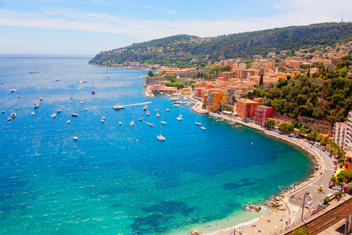 Eine kurvenreiche Küstenstraße führt entlang der tiefblauen Bucht von Saint-Tropez mit mediterraner Vegetation