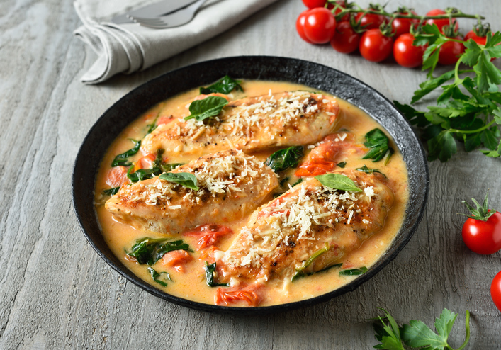 Eine Pfanne mit gebratenem Hähnchen, Spinat und Kirschtomaten in einer hellen Sauce, typisch für die Toskana.
