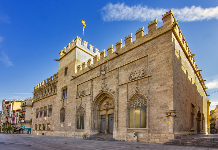 Das historische Gebäude der Lonja de la Seda in Valencia mit Zinnen und einer Flagge unter blauem Himmel.