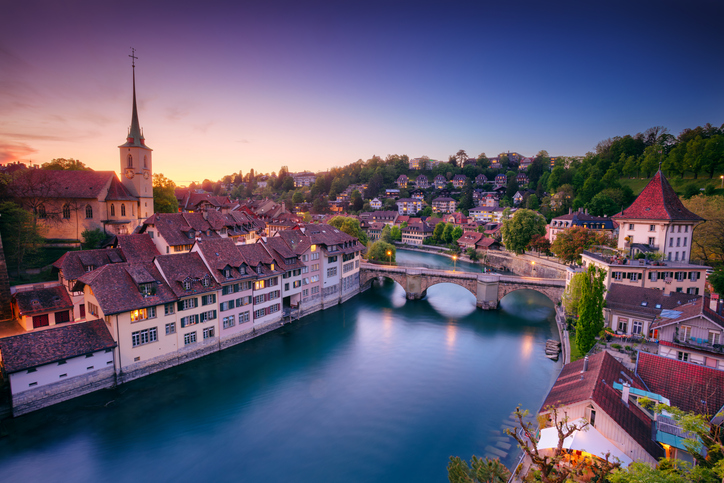 Die beleuchtete Berner Altstadt spiegelt sich bei Sonnenuntergang im Wasser der Aare