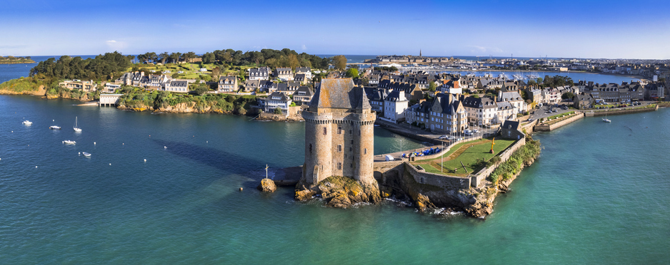 Ein markanter dreifacher Turm aus Stein auf einer kleinen Felsnase im Wasser, im Hintergrund die Häuserzeile des Stadtteils Saint-Servan.
