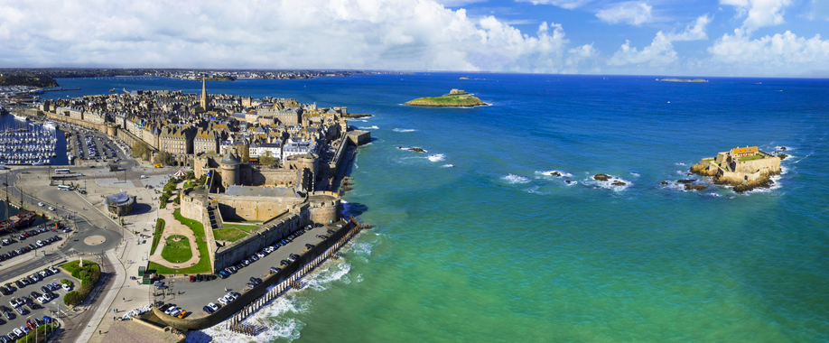 Eine weite Panorama-Luftaufnahme der befestigten Altstadt von Saint-Malo direkt am Meer, daneben eine kleine Festungsinsel im Wasser.