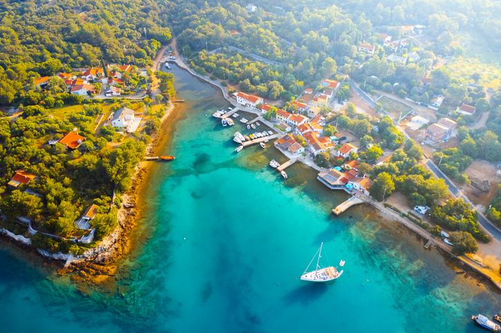 Drohnenaufnahme eines kleinen Fischerdorfes auf Cres, das in einer tiefen Bucht mit kristallklarem Wasser liegt.
