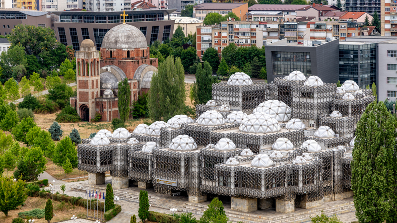 Die moderne Nationalbibliothek des Kosovo mit ihren markanten Kuppeln steht in Pristina neben einer traditionellen Backsteinkirche.