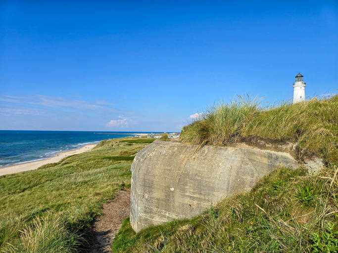Ein alter Betonbunker aus dem Zweiten Weltkrieg steht in den Dünen vor dem weißen Leuchtturm in Hirtshals