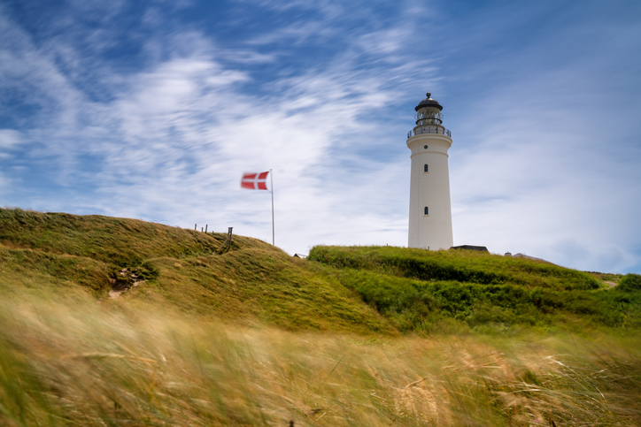 Der Hirtshals Fyr ragt vor einem blauen Himmel über den windgepeitschten Dünengräsern auf