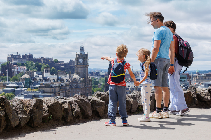 Familie mit Kindern betrachtet den Blick auf Edinburghs Wahrzeichen und den Clock Tower von einem Aussichtspunkt aus
