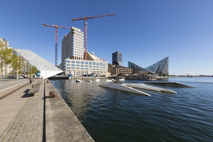 Eine Baustelle in Aarhus Ø mit großen Kränen, modernen Glasfassaden und einer Promenade am Wasser.