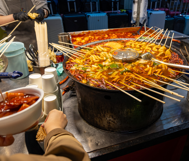 Ein großer Topf mit scharfem Tteokbokki und Fischkuchen auf einem Marktstand, bereit für die hungrigen Gäste.