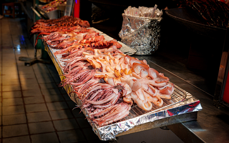 Verschiedene Tintenfische und Oktopusse liegen auf einem Metallgrill an einem Streetfood-Stand in Südkorea.