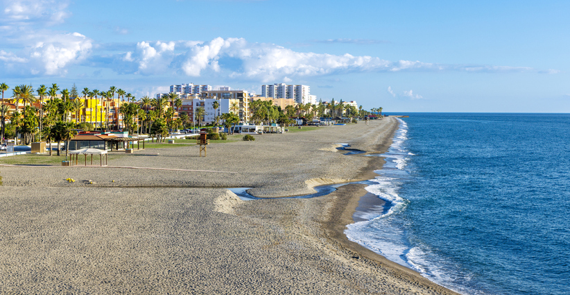 Ein breiter Kieselstrand an der Costa Tropical mit Blick auf das azurblaue Meer und die angrenzende Stadt.