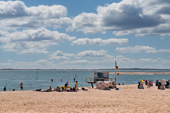 Ein weiter Sandstrand in Hörnum mit Strandkörben, einer Rettungsschwimmerstation und Menschen, die das sonnige Wetter an der Nordsee genießen.