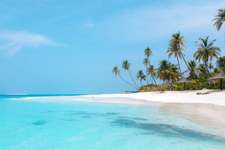 Weißer Sandstrand mit schiefen Palmen und türkisblauem Meer bei strahlendem Sonnenschein