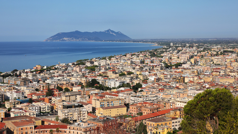 Eine weite Aufnahme der Stadt Terracina am Meer, am Horizont zeichnet sich die markante Silhouette des Berges Monte Circeo ab.