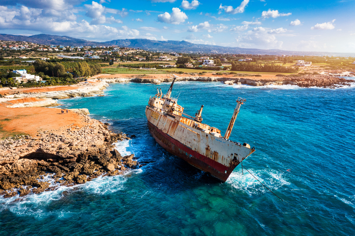 Ein großes, rostiges Frachtschiff liegt in Schräglage direkt vor der zerklüfteten Felsküste im Meer.