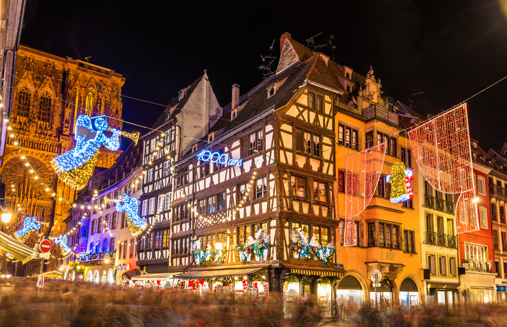 Ein beleuchteter Platz in der Nacht mit Weihnachtsdekorationen, Lichterketten und dem Straßburger Münster im Hintergrund.