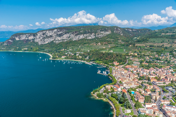 Blick aus der Luft auf die grüne Küstenlinie und die dichte Bebauung einer Stadt direkt am Gardasee.