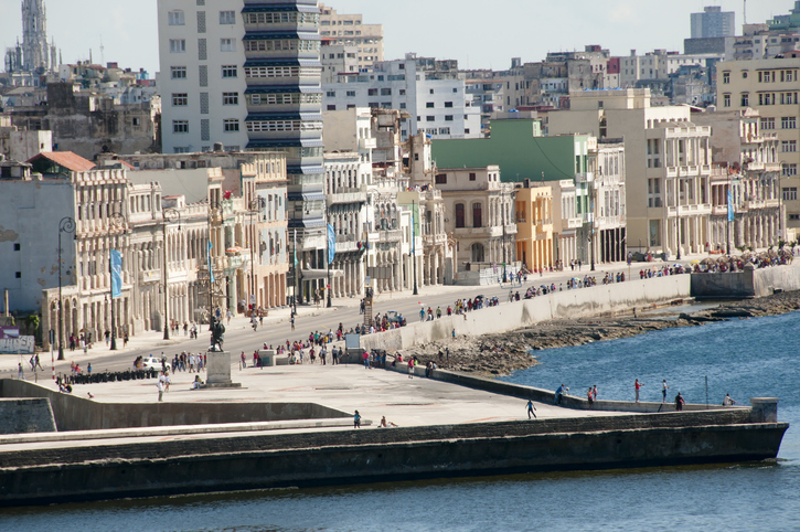 Blick von oben auf die langgezogene Malecón-Promenade in Havanna mit vielen Menschen, die am Meer entlang spazieren.
