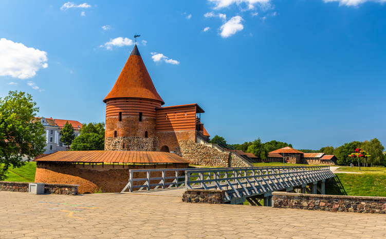 Eine gut erhaltene Backsteinburg mit einem markanten runden Turm und kegelförmigem Dach unter strahlend blauem Himmel.