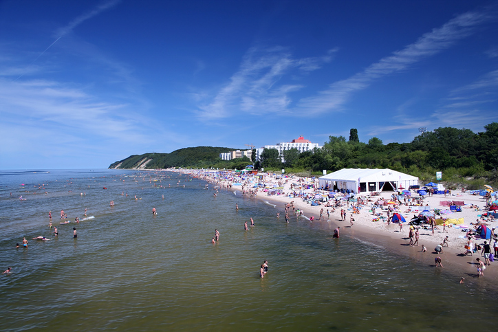 Ein sonniger Sommertag am Strand von Misdroy mit zahlreichen Badegästen, weißen Zelten und strahlend blauem Himmel.