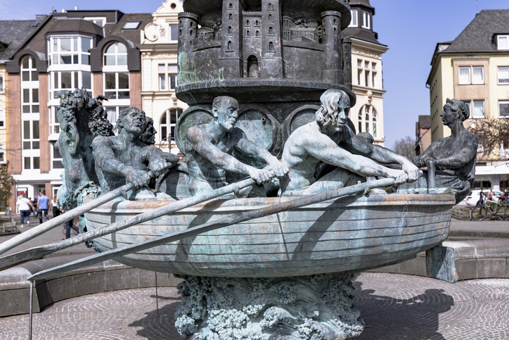 Detailansicht einer bronzenen Brunnenskulptur, die Männer in einem Boot beim Rudern zeigt, Teil einer großen Säule.