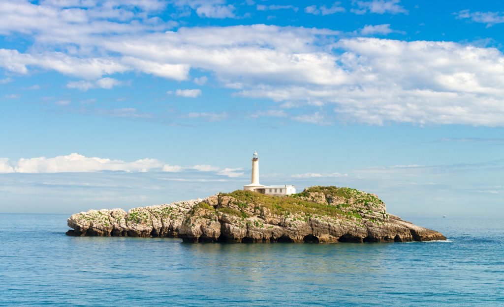 Ein einsamer weißer Leuchtturm steht auf einer felsigen Insel inmitten des tiefblauen Ozeans.