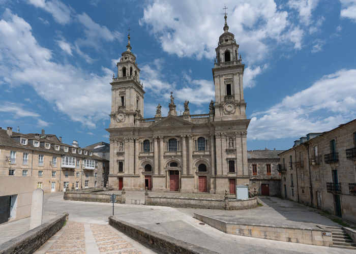 Die kunstvolle Steinfassade der Kathedrale erstreckt sich zwischen zwei symmetrischen Türmen unter einem sonnigen, blau-weißen Himmel.