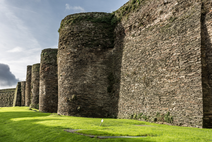 Massive, abgerundete Steinbastionen der antiken Stadtmauer erheben sich über einer gepflegten grünen Wiese.