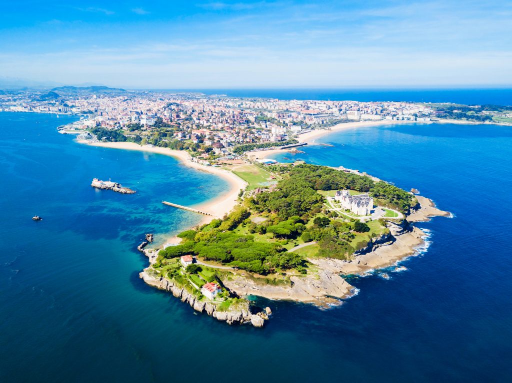 Eine grüne Halbinsel ragt ins blaue Meer, an deren Spitze ein historischer Palast steht.