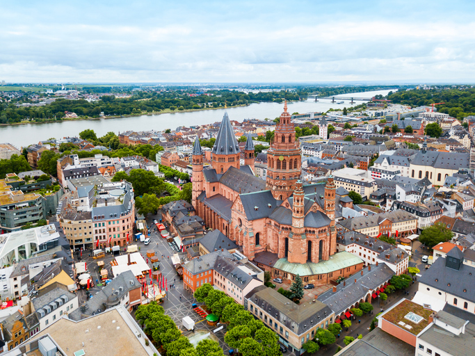 Eine beeindruckende Vogelperspektive zeigt den monumentalen Mainzer Dom mitten in der bebauten Stadt, umgeben von Bäumen und angrenzenden Straßen.