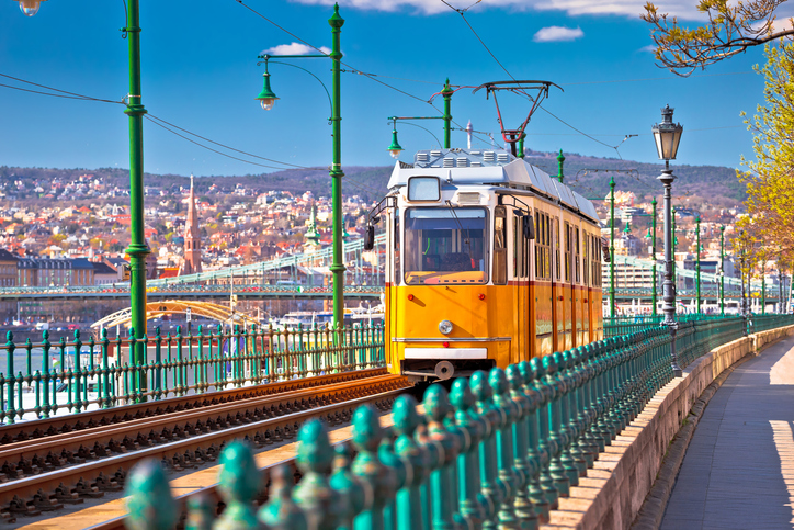 Eine gelbe Straßenbahn fährt über eine Brücke mit grünem Geländer in Budapest.