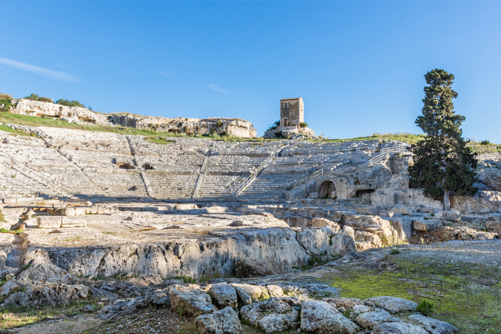 Das antike griechische Theater in Syrakus, eingebettet in die felsige Landschaft mit einem einsamen Baum daneben.
