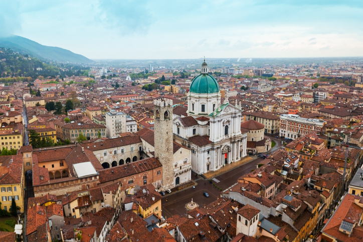 Eine weite Luftaufnahme über das historische Stadtzentrum von Brescia mit der beeindruckenden Kathedrale und den umliegenden roten Ziegeldächern.